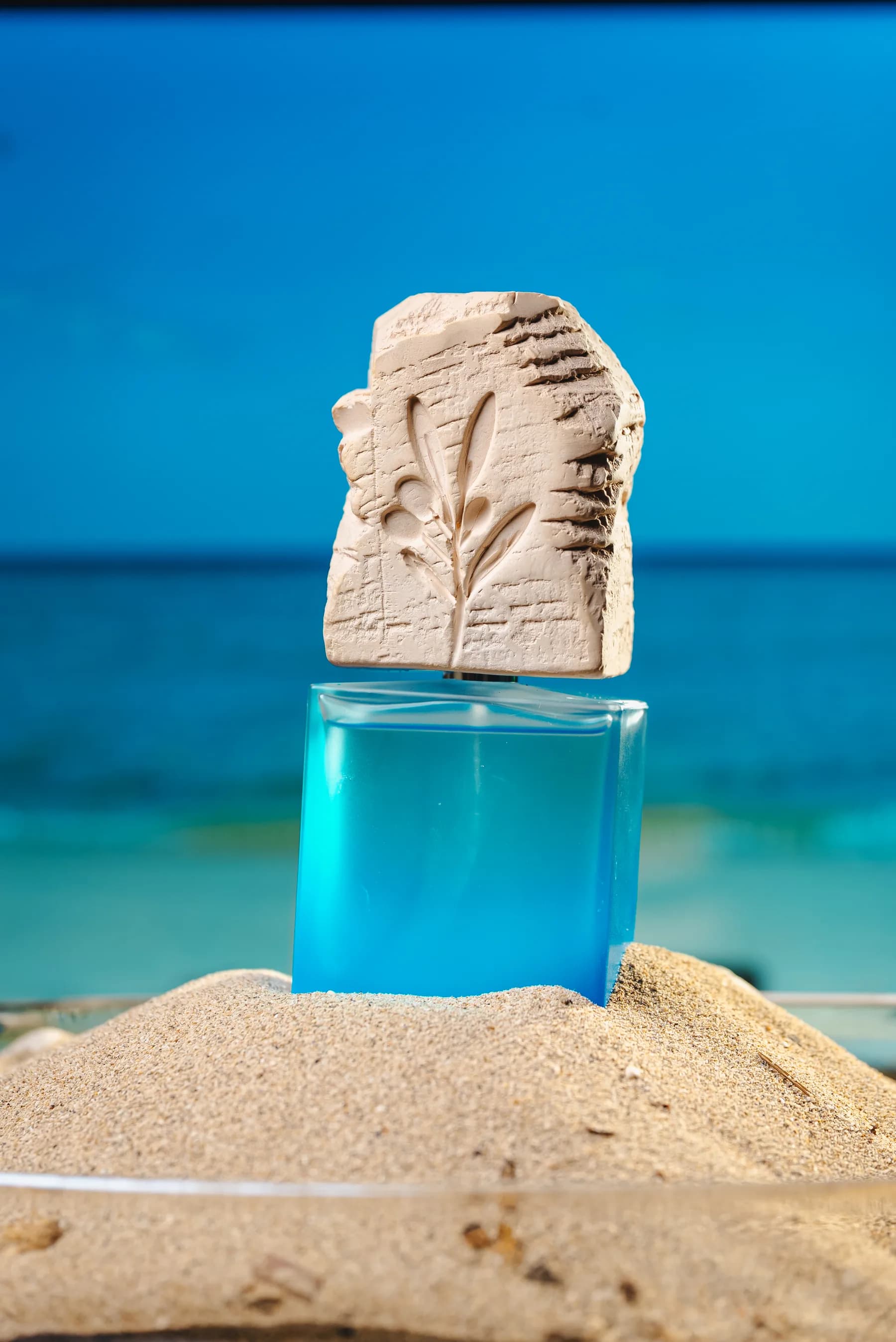 Flacone azzurro con scultura in pietra sulla sabbia davanti al mare.