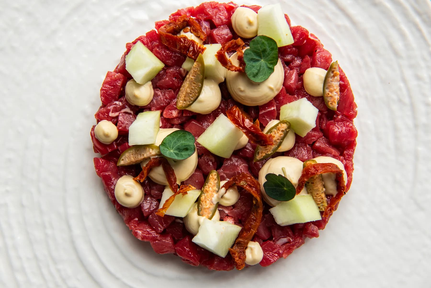 Tartare di tonno con melone, fichi e crema in piatto texturizzato.