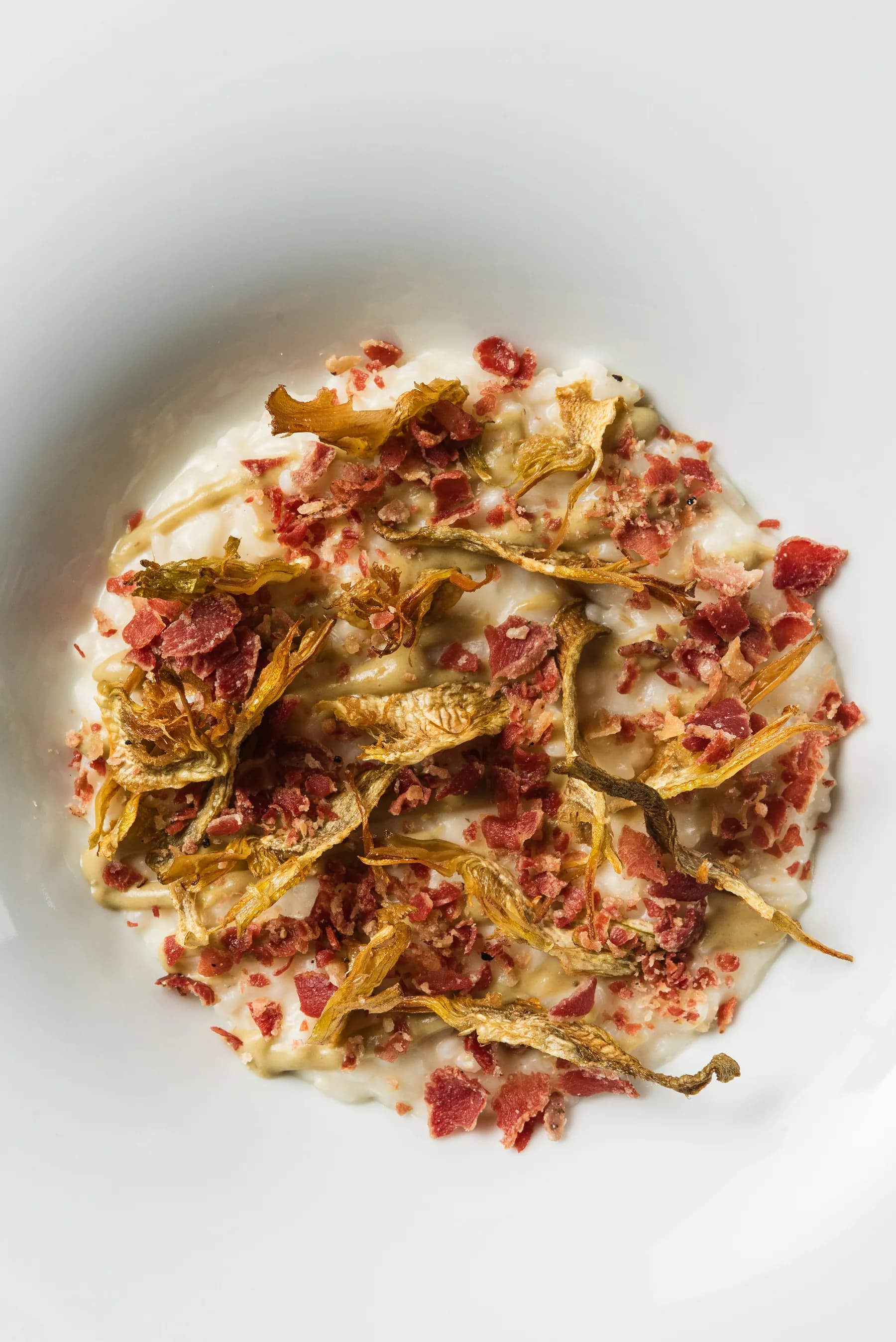 Piatto di carciofi croccanti con pancetta su crema bianca.