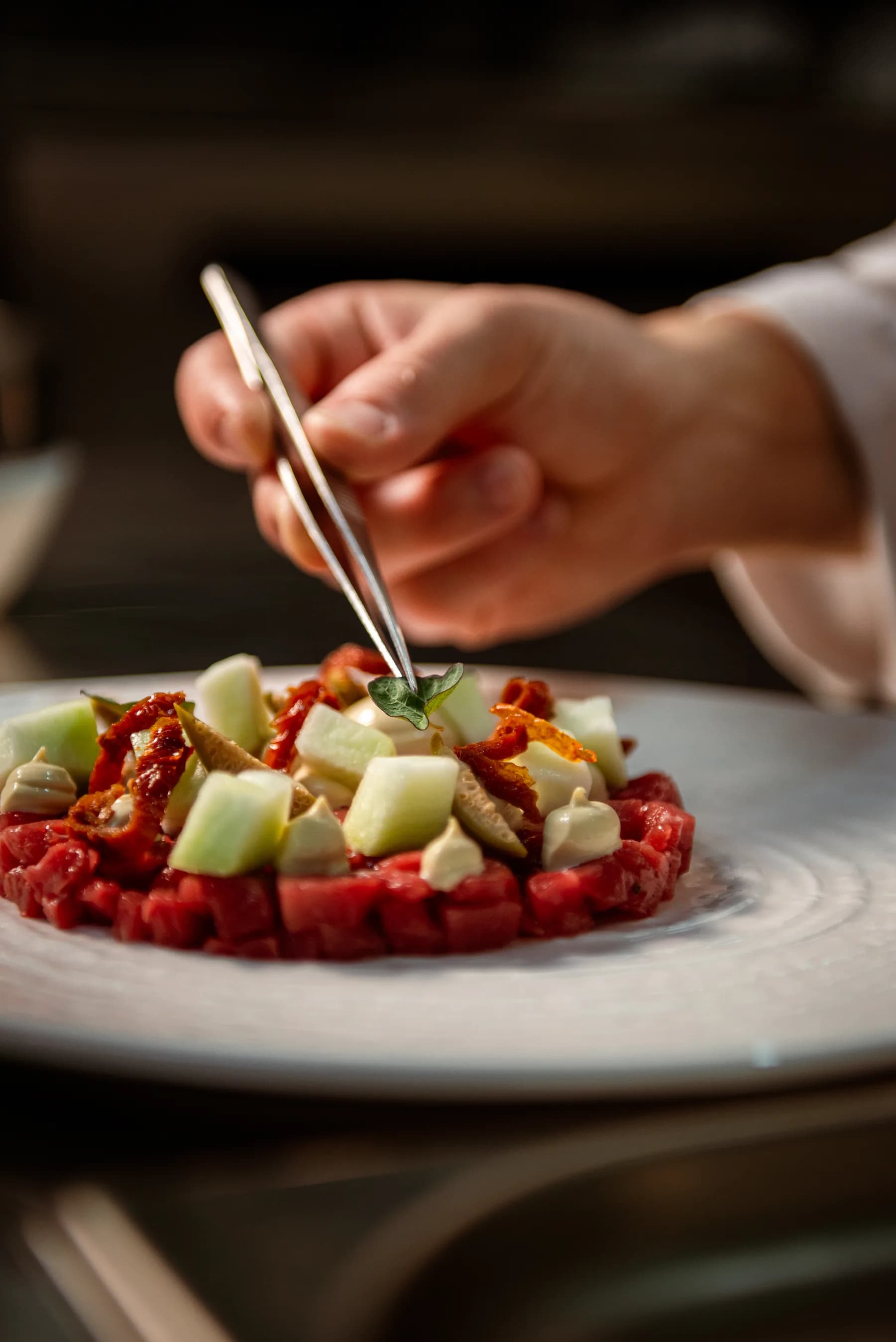 Chef impiatta una tartare con la pinzetta.