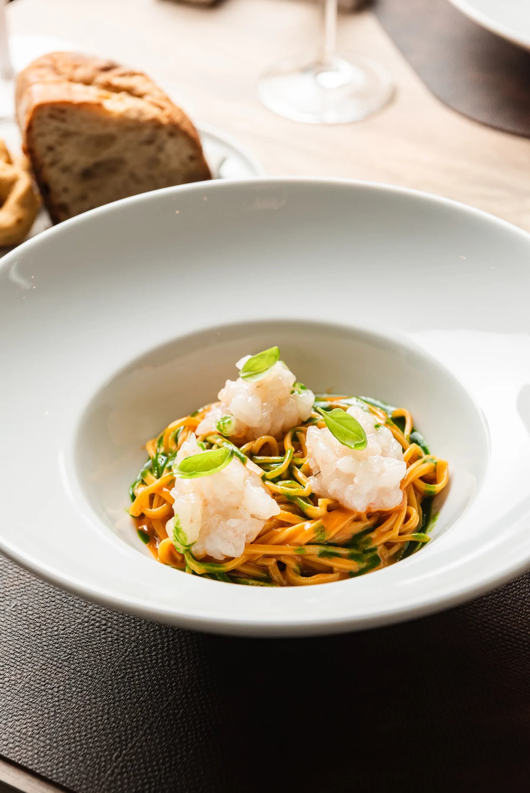 Pasta con gamberi e verdure su piatto fondo bianco.
