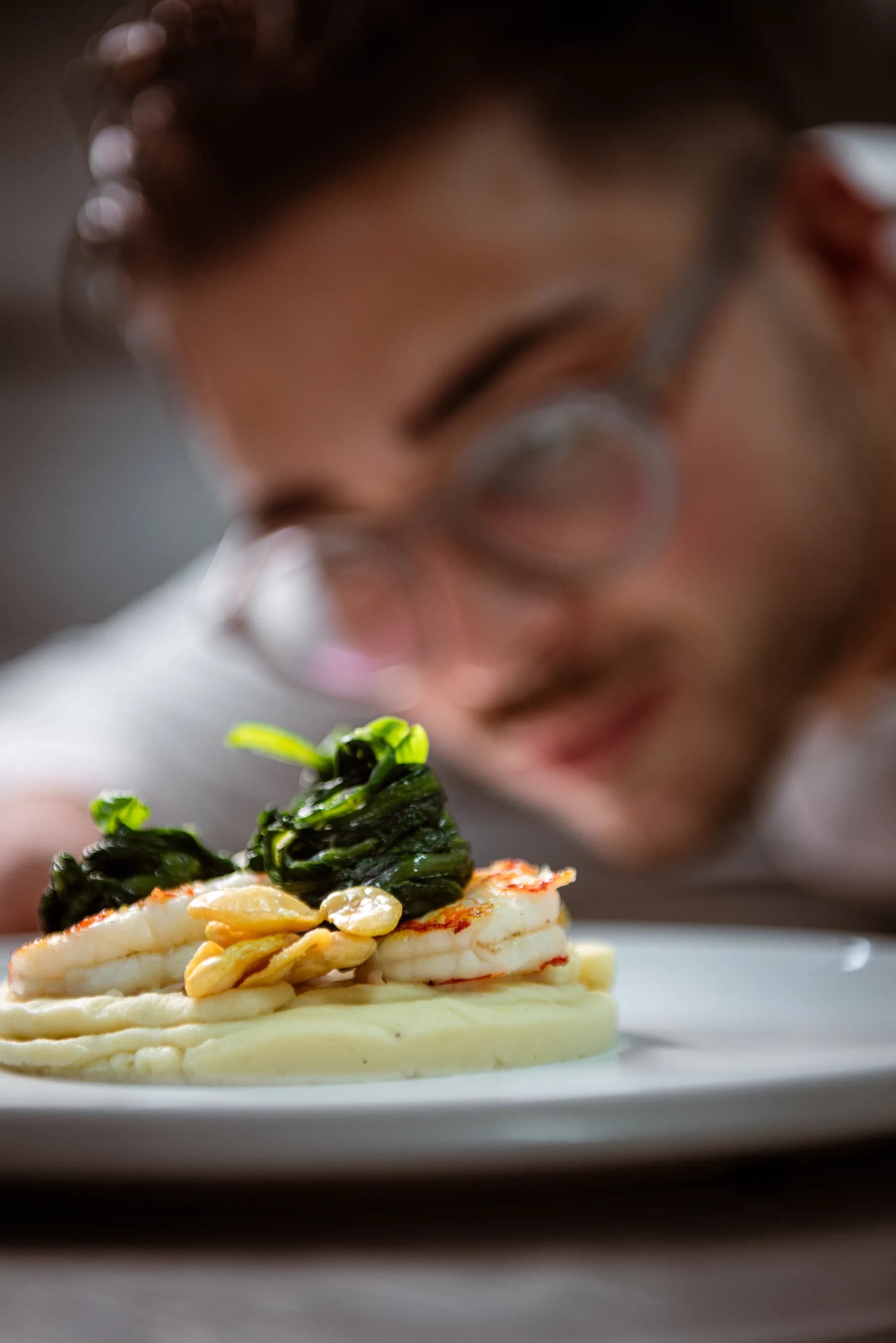 Chef concentrato sull'impiattamento di un piatto di pesce con spinaci.