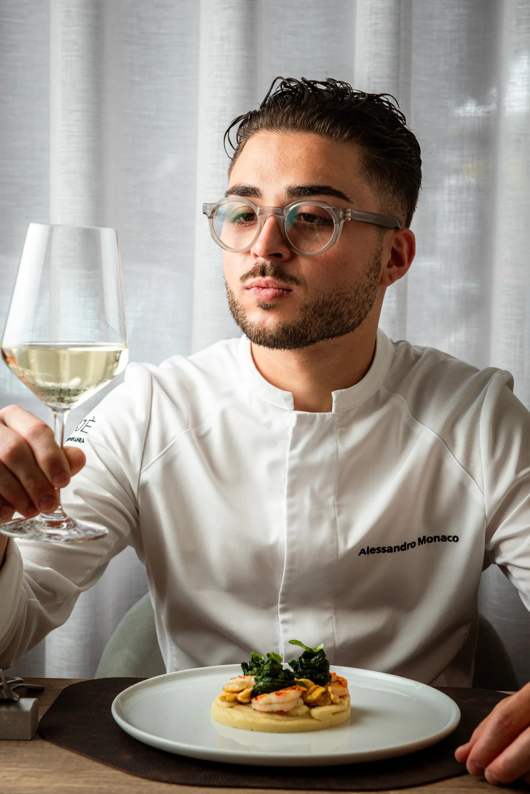 Chef con il calice di vino bianco davanti a un piatto.