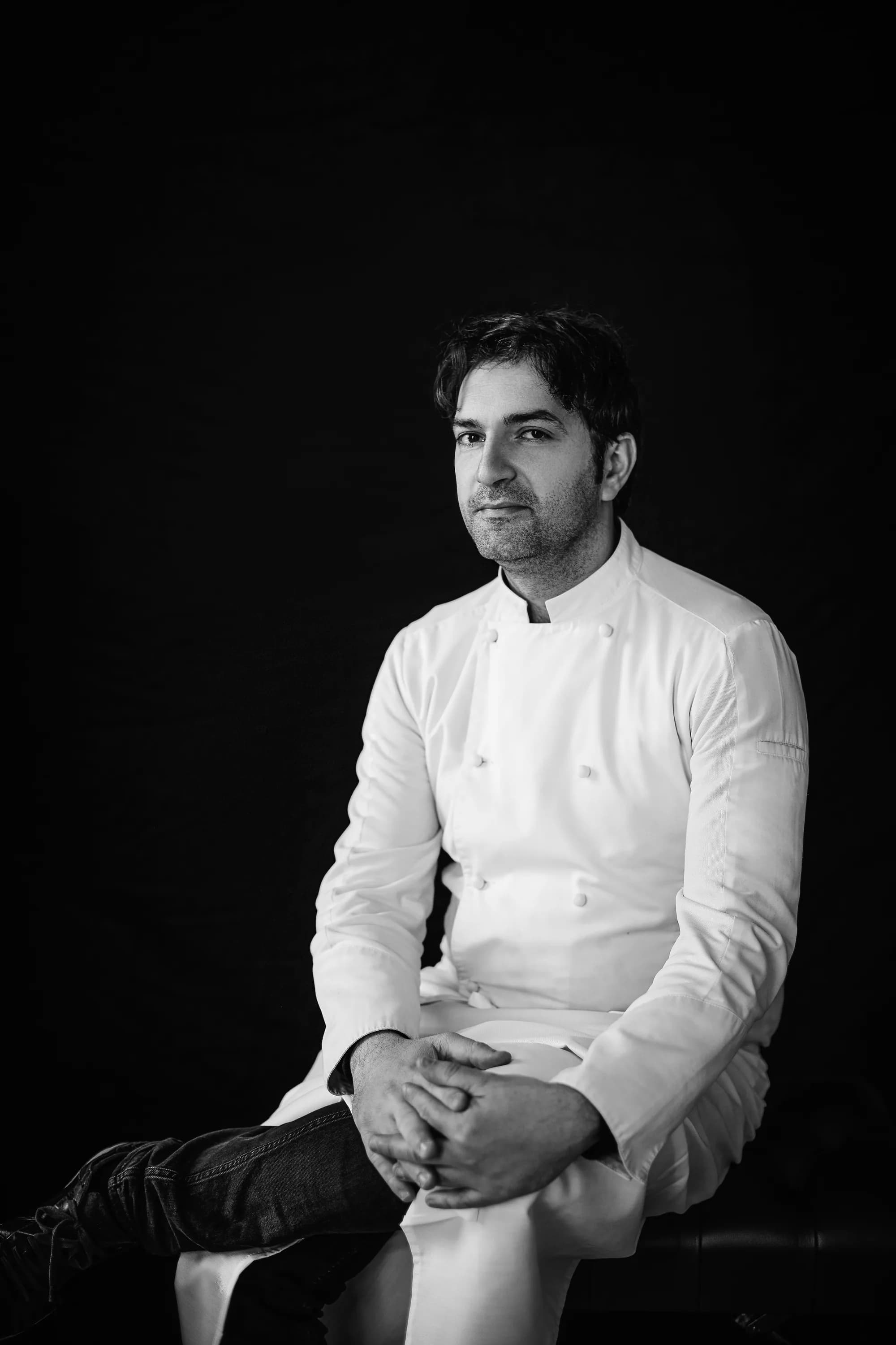 Ritratto in bianco e nero dello chef Martino Ruggieri seduto su fondo nero.