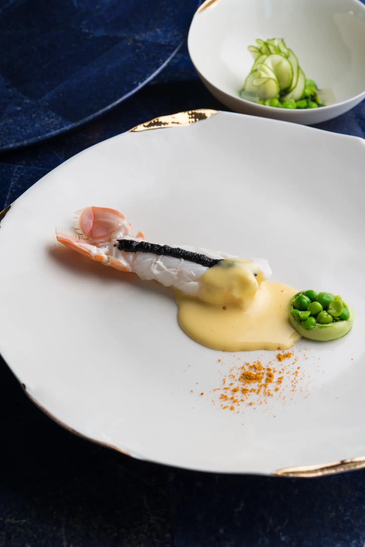 Piatto di crostaceo con crema e piselli su fondo blu.
