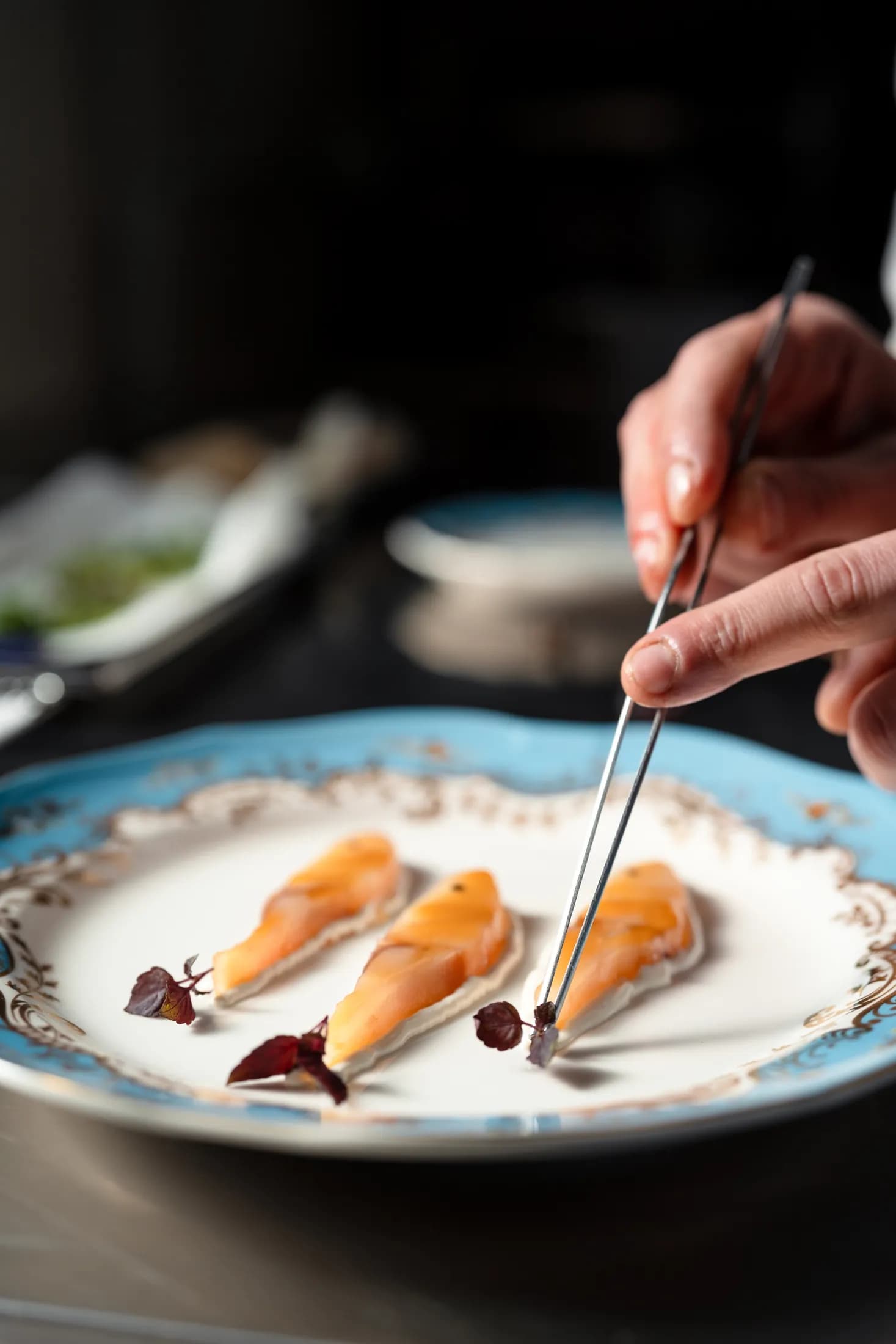 Chef impiatta con la pinzetta su porcellana azzurra.