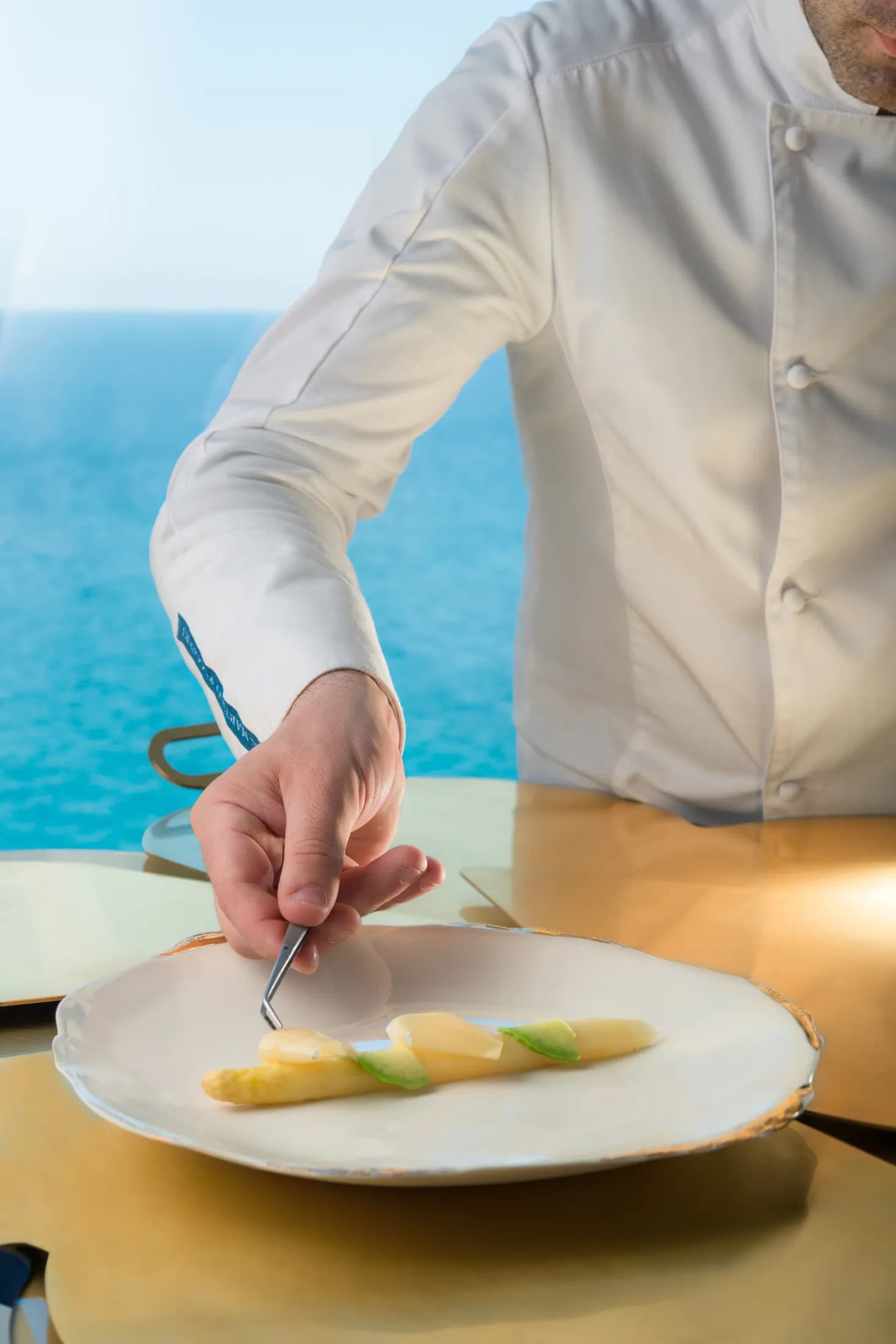 Gesto dello chef che completa un piatto con il mare alle spalle.