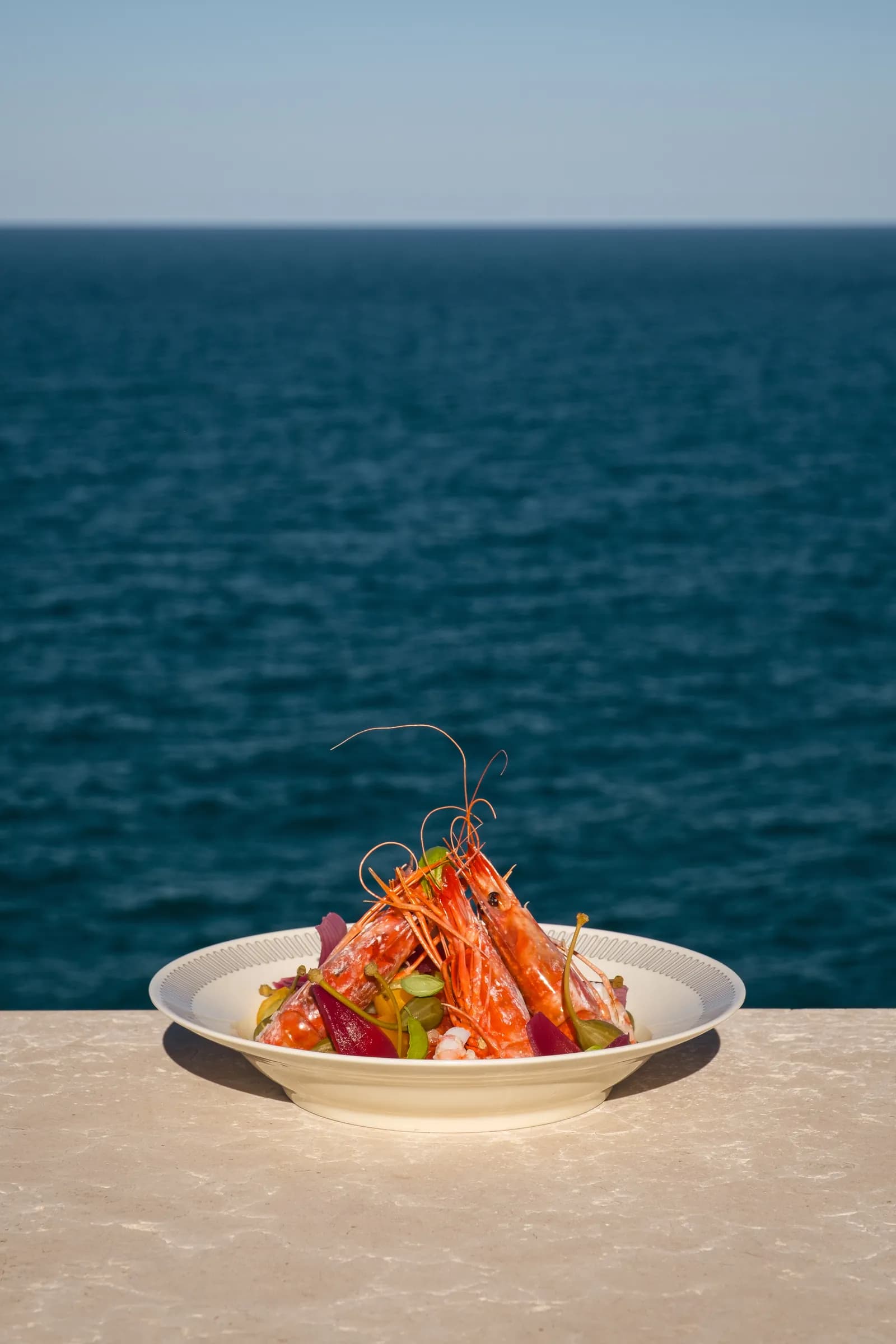 Crudo di gamberi Morus servito con il mare sullo sfondo.