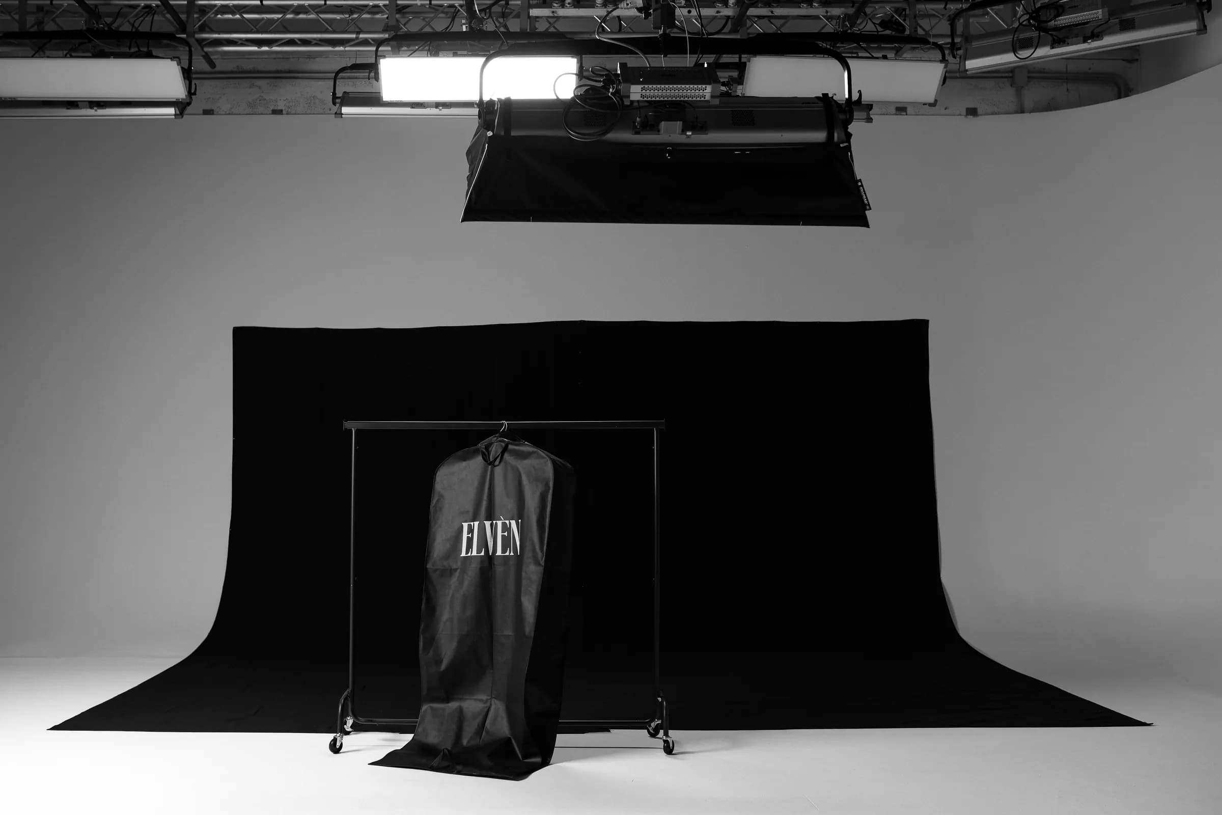 Set fotografico ELVÈN con garment bag brandizzata su fondale nero.