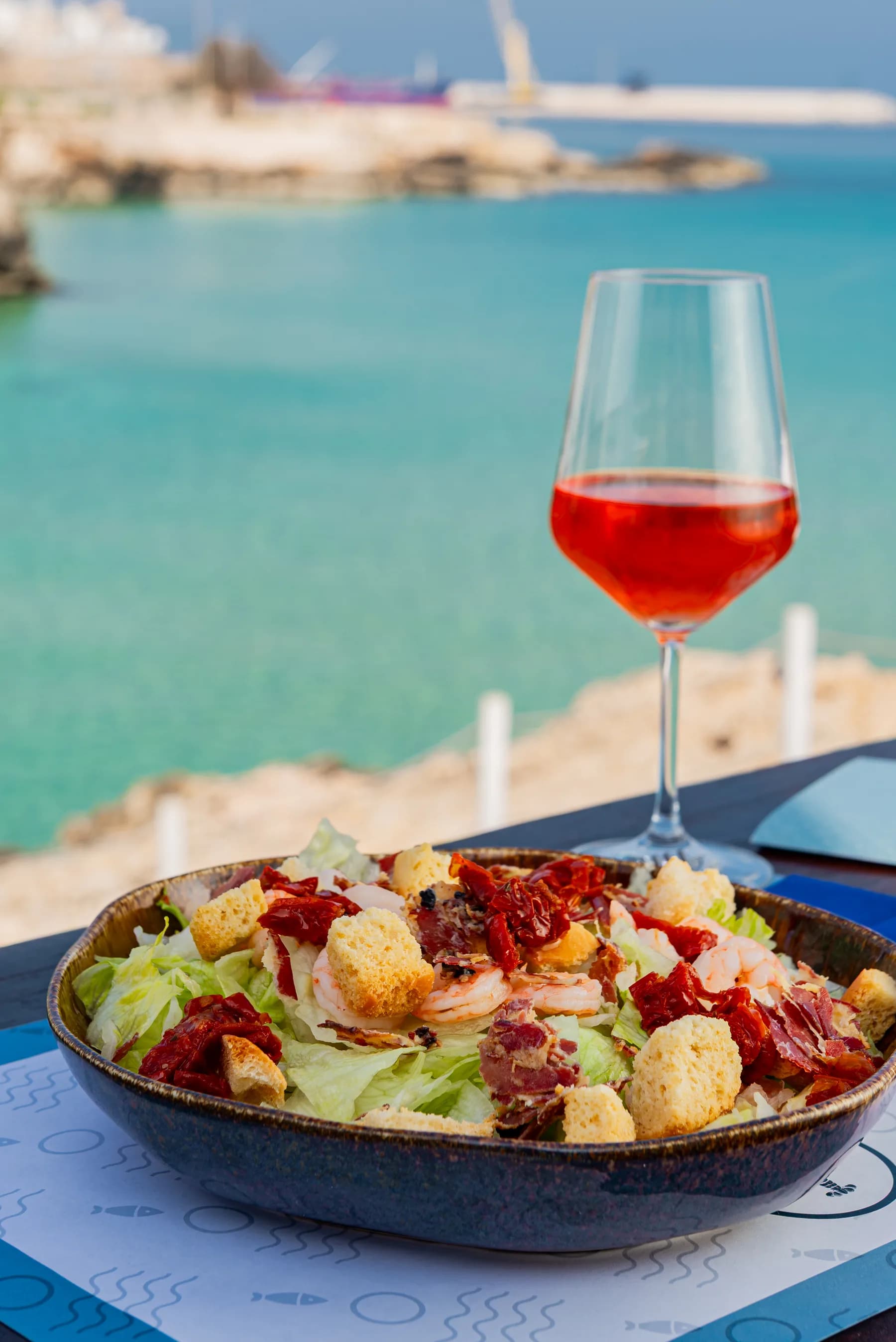 Insalata con gamberi e speck su un tavolo con vista sul mare.